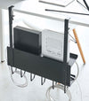 Back view of black Wall-Mount Cable and Router Storage Rack hanging from desk by Yamazaki Home.