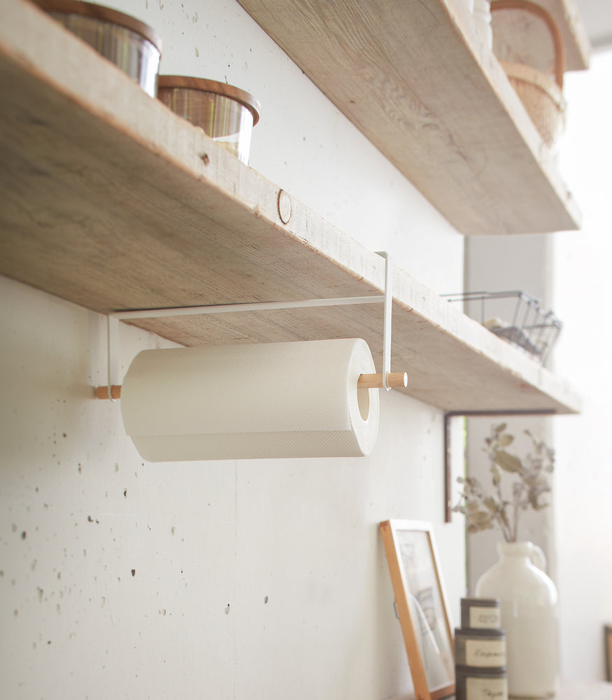View 2 - Side view of white Undershelf Organizer in kitchen holding paper towel by Yamazaki Home.