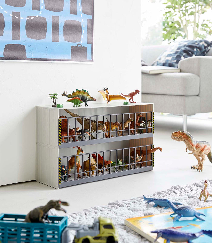 View 2 - White Two-Tier Toy Dinosaur and Animal Storage Rack in living room play area holding toy dinosaurs by Yamazaki Home.