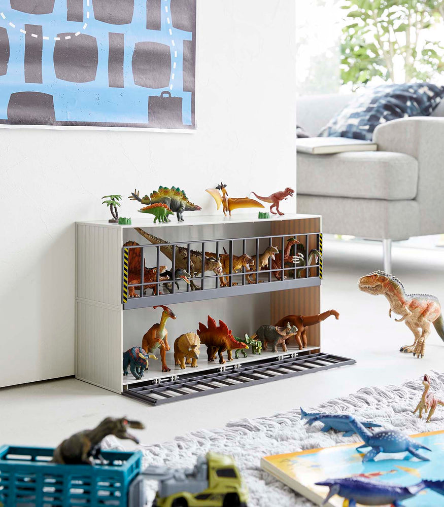 View 3 - White Two-Tier Toy Dinosaur and Animal Storage Rack in living room play area holding toy dinosaurs by Yamazaki Home.