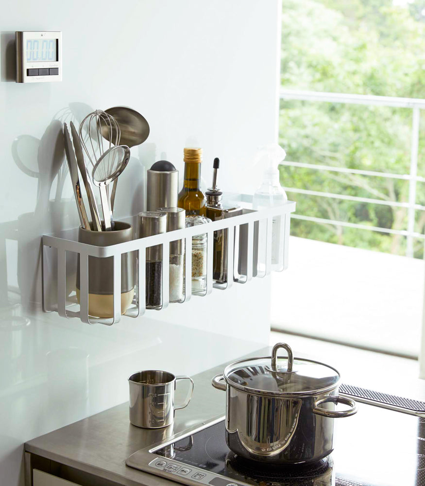 View 2 - White Magnetic Storage Basket holding spices, oils, and utensils in kitchen by Yamazaki Home.