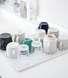 White Dish Drainer Tray holding cups on sink countertop by Yamazaki Home.