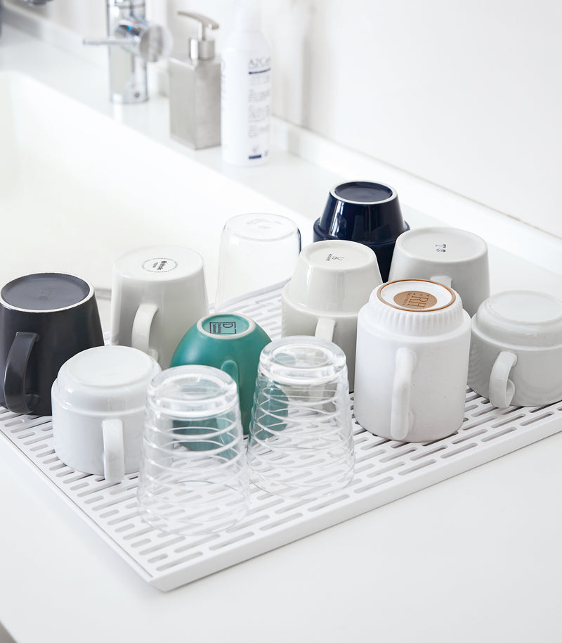 White Dish Drainer Tray holding cups on sink countertop by Yamazaki Home.
