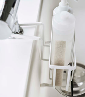 Close up side view of Yamazaki Home white Faucet-Hanging Sponge Caddy attached to a kitchen sink view 6