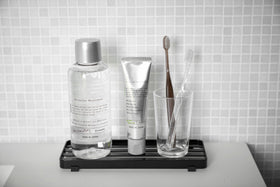 Front view of black Slotted Tray holding toothpaste, mouthwash, and toothpaste on bathroom counter by Yamazaki Home. view 8