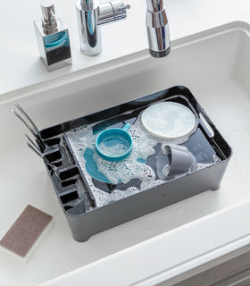 Black Dish Rack in kitchen sink holding water and dishes by Yamazaki Home. view 12