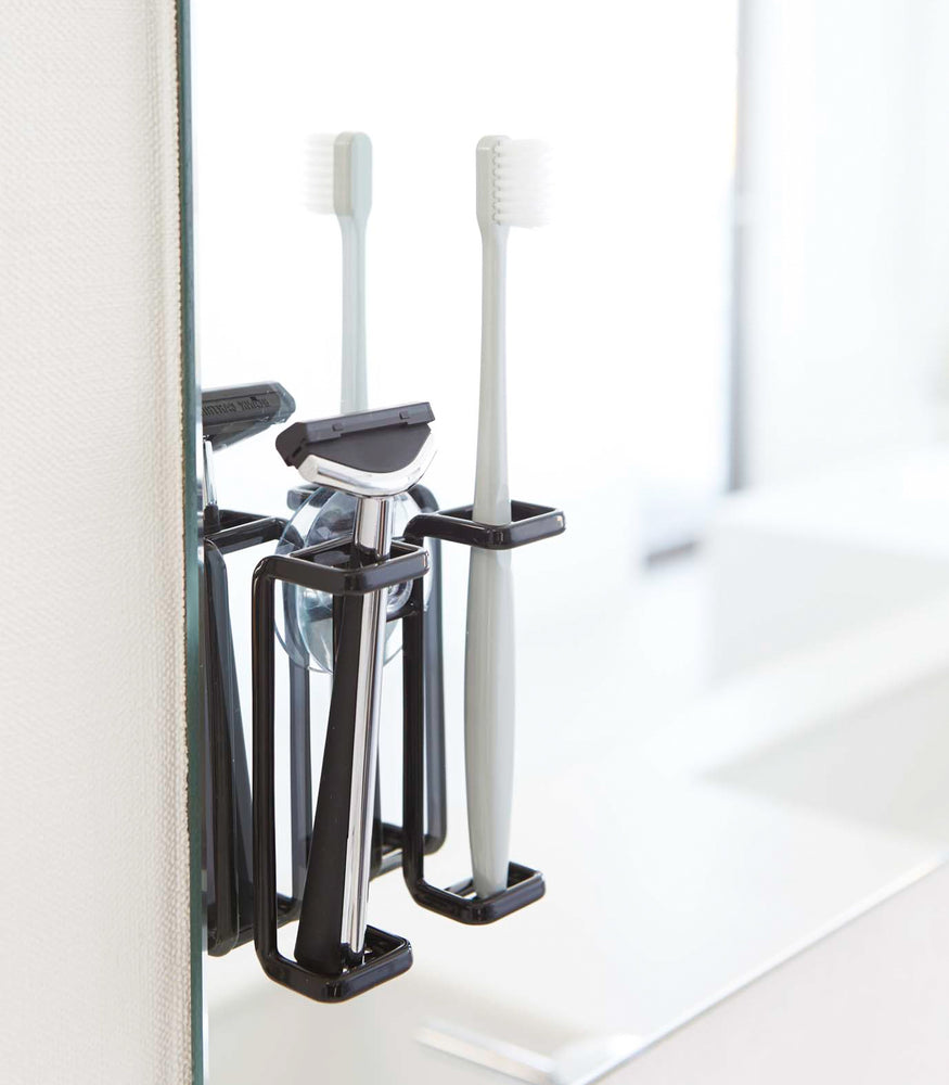 View 5 - Black Toothbrush Holder holding toothbrush and razor on bathroom mirror by Yamazaki Home.