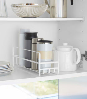 Yamazaki Home white Glass and Mug Cabinet Organizer on a shelf beside a tea pot and plates view 1