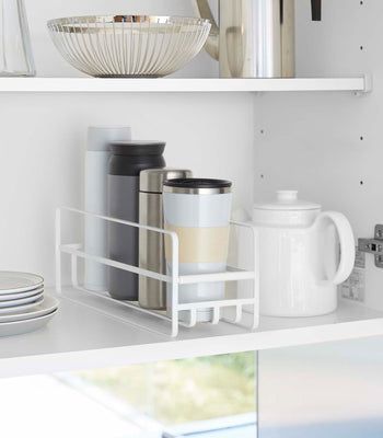 Yamazaki Home white Glass and Mug Cabinet Organizer on a shelf beside a tea pot and plates