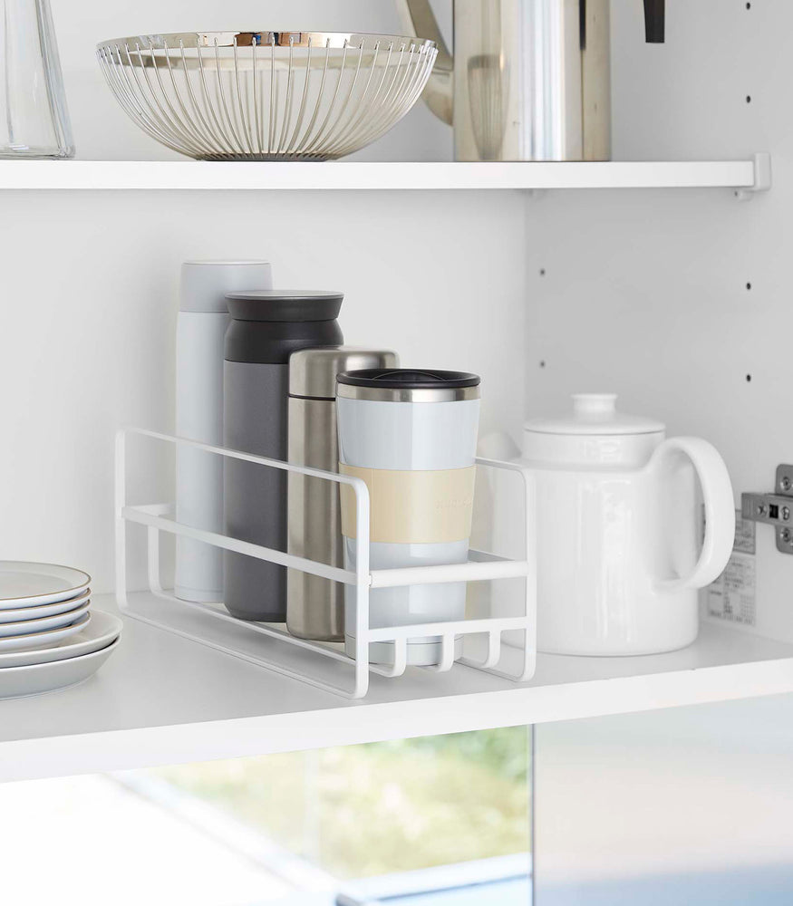 View 1 - Yamazaki Home white Glass and Mug Cabinet Organizer on a shelf beside a tea pot and plates