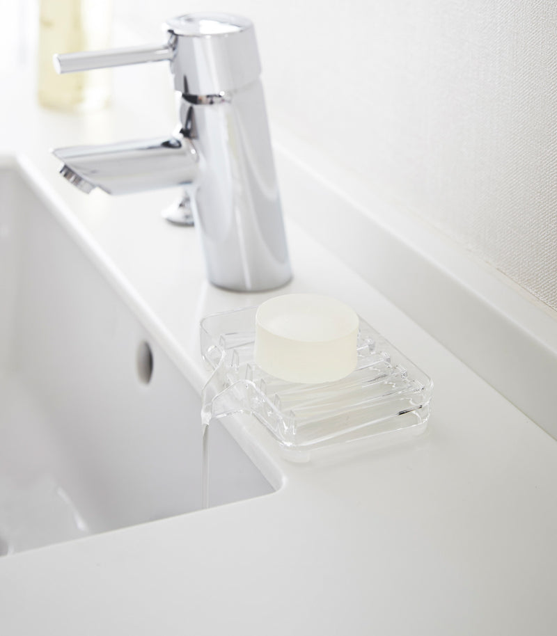 Clear Self-Draining Soap Tray holding soap on sink counter by Yamazaki Home.