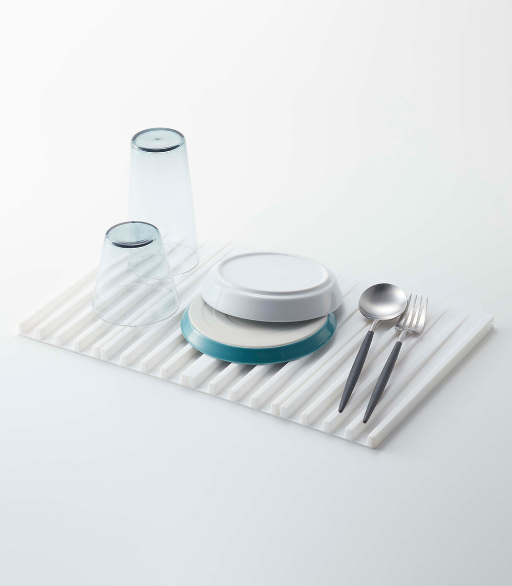 White Folding Dish Drainer Mat holding dishware on white background by Yamazaki Home.