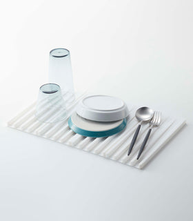 White Folding Dish Drainer Mat holding dishware on white background by Yamazaki Home. view 2