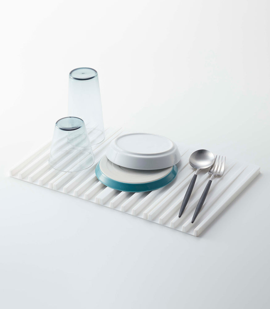 View 2 - White Folding Dish Drainer Mat holding dishware on white background by Yamazaki Home.