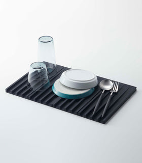 Black Folding Dish Drainer Mat holding dishware on white background by Yamazaki Home. view 7