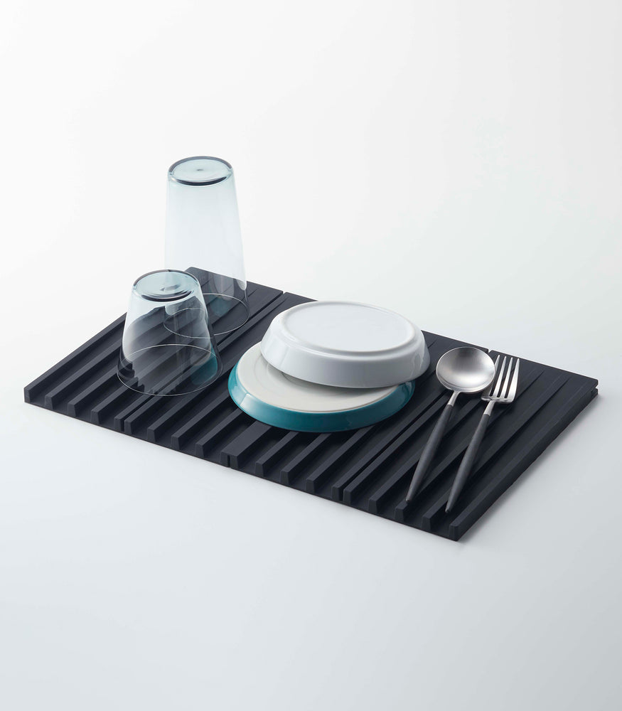 View 7 - Black Folding Dish Drainer Mat holding dishware on white background by Yamazaki Home.