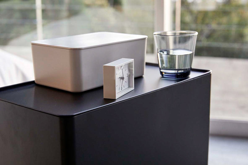 Close up view of black Rolling Diaper Stacker displaying clock, glass, and wet wipe dispenser by Yamazaki Home.