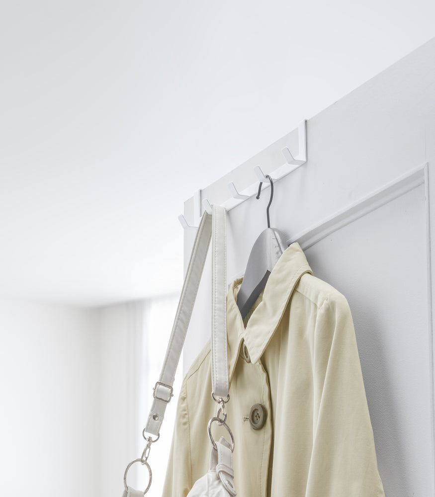 View 5 - White Over-the-Door Hanger holding bag and jacket on door by Yamazaki Home.