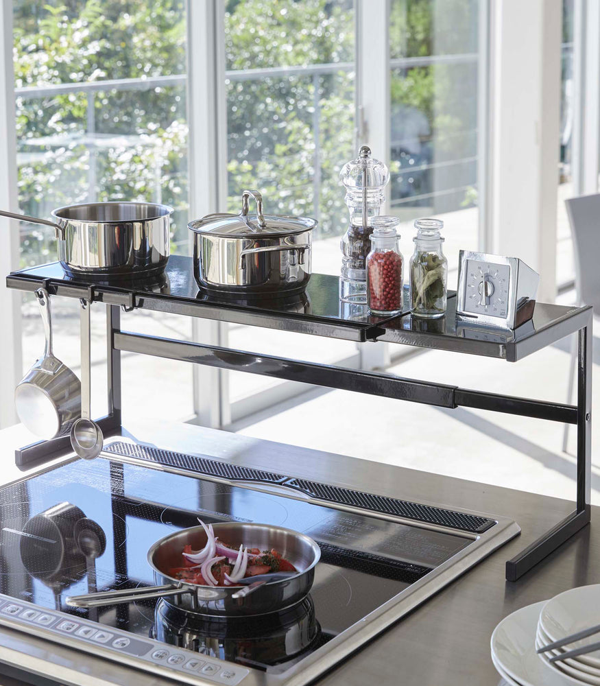View 15 - Black Expandable Kitchen Support Rack holding kitchen items over stovetop by Yamazaki Home.