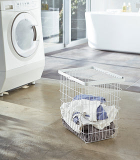 White Wire Laundry Basket holding clothes in laundry room by Yamazaki Home. view 2