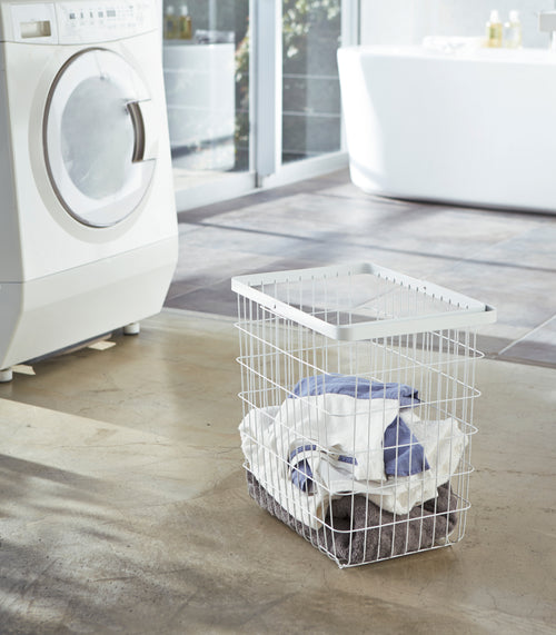 White Wire Laundry Basket holding clothes in laundry room by Yamazaki Home.