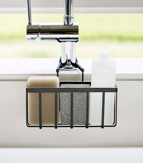Close up frontal view of a Yamazaki Home black Faucet-Hanging Sponge Caddy in a sink view 11