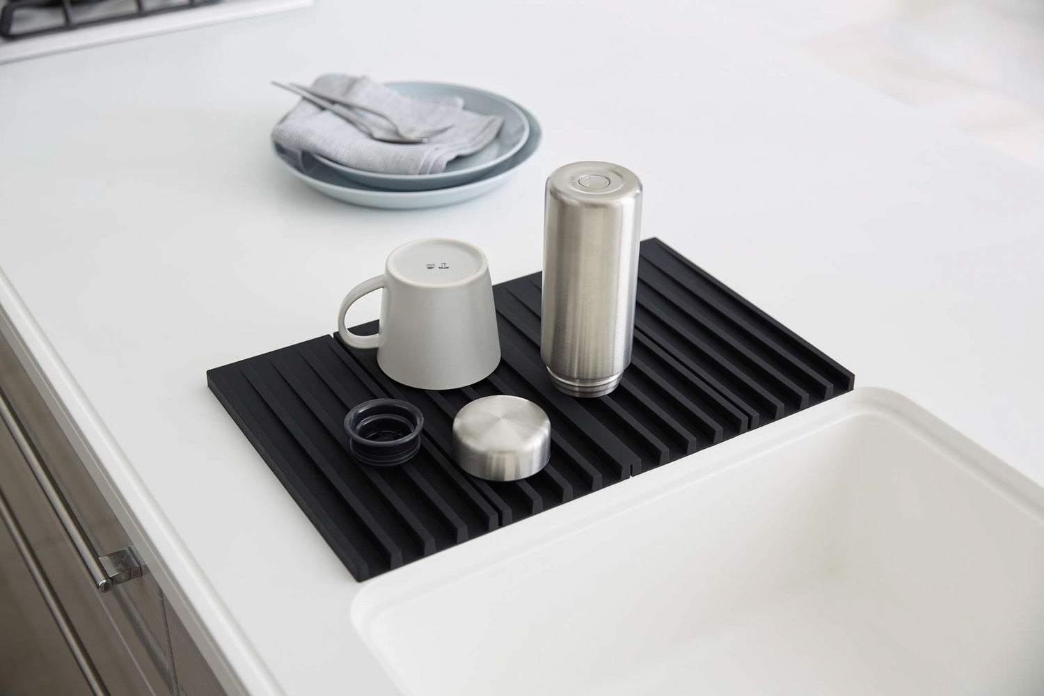 View 10 - Black Folding Dish Drainer Mat holding cup and bottle on sink counter by Yamazaki Home.