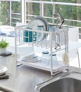 White Two-Tier Dish Rack holding plates, cups, and silverwear next to kitchen sink by Yamazaki Home. view 3
