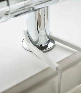 Close up of Yamazaki Home white Faucet-Hanging Sponge Caddy attached to a sink view 7