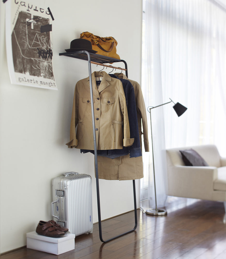View 4 - Black Leaning Coat Rack with Shelf holding hat, bag, and jackets in living room by Yamazaki Home.