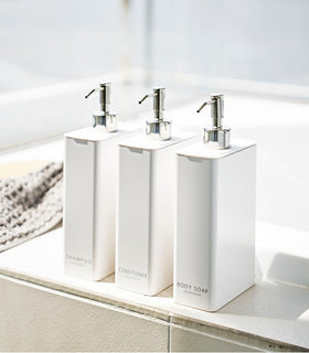 Yamazaki Home white Shampoo, Conditioner, and Body Soap dispensers next to the bathtub. view 2
