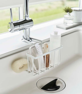Yamazaki Home white Faucet-Hanging Sponge Caddy attached to a kitchen sink view 2