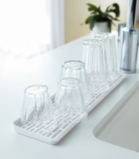 Side view of white Sink Drainer Tray holding glasses on sink counter by Yamazaki Home. view 6