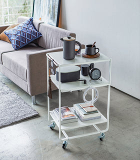 White Rolling Utility Cart holding books and gadgets in living room by Yamazaki Home. view 5