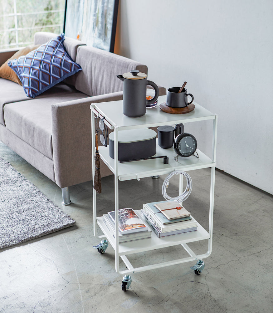 View 5 - White Rolling Utility Cart holding books and gadgets in living room by Yamazaki Home.