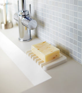 White Self-Draining Soap Tray holding soap on sink counter by Yamazaki Home. view 3