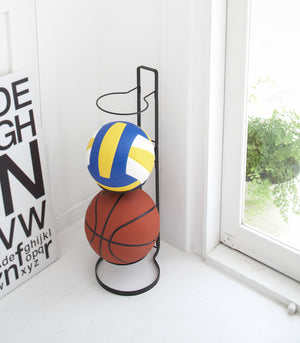 Black Sport Ball Stand holding sport balls in bedroom by Yamazaki Home.