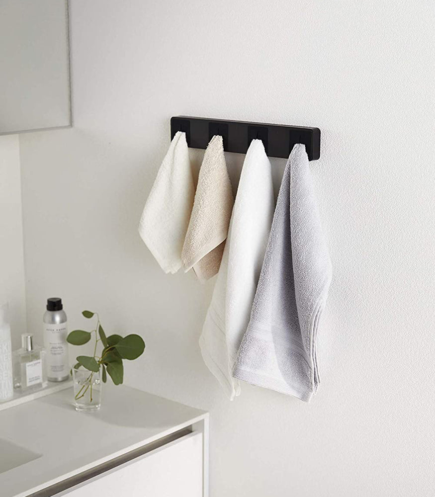 View 8 - Black Push Dish Towel Holder holding towels on bathroom wall by Yamazaki Home.