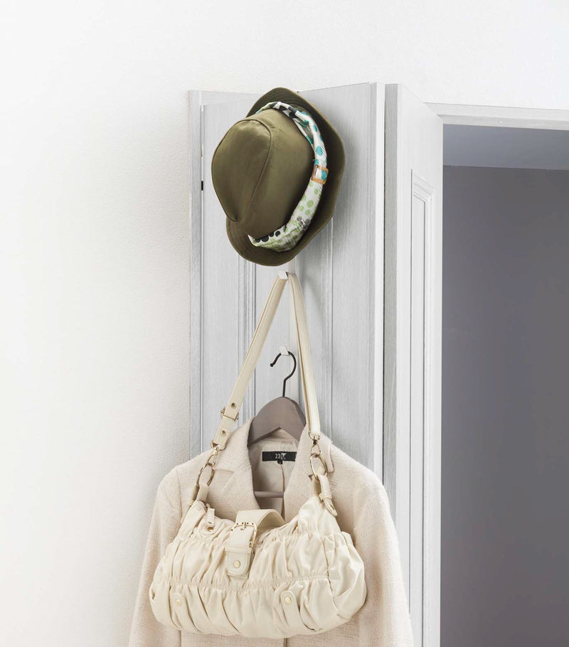 White Over-the-Door Hanger displaying hat, purse, and jacket on door by Yamazaki Home.