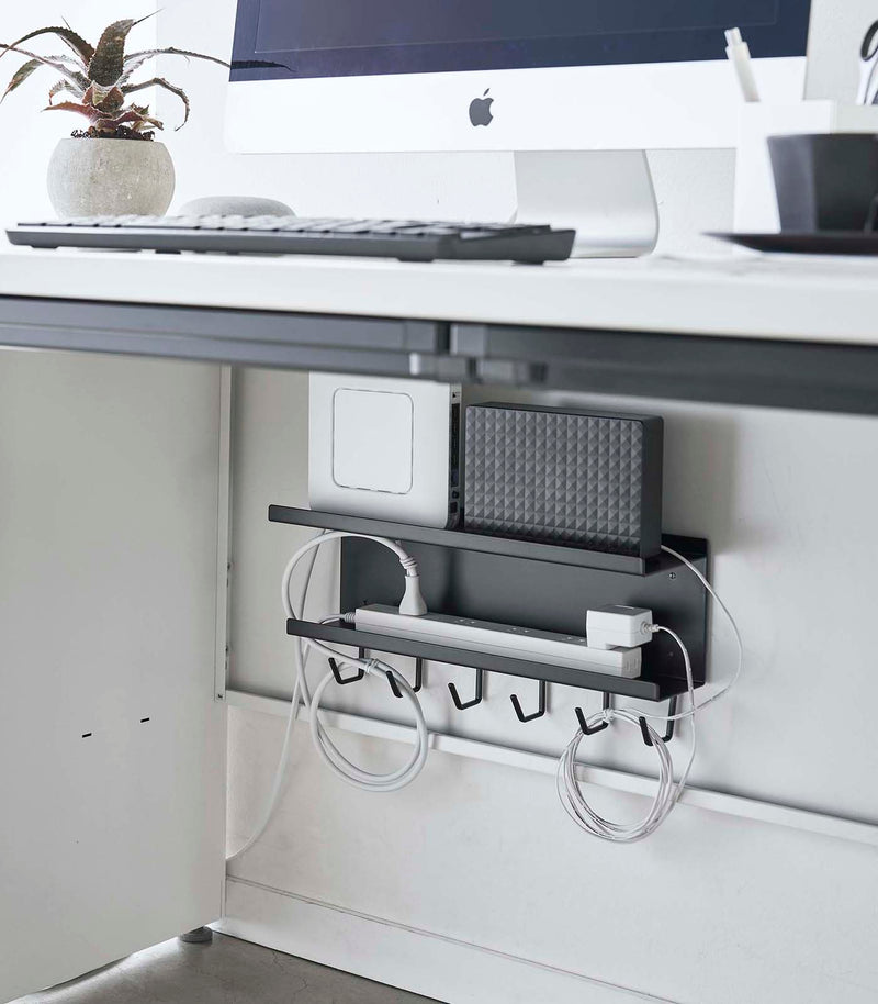 Black Wall-Mount Cable and Router Storage Rack holding routers and power cord under desk by Yamazaki Home.