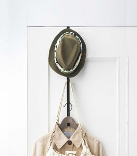 Black Over-the-Door Hanger displaying hat, purse, and jacket on closet door by Yamazaki Home. view 8