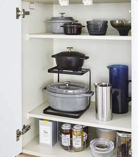 Front view of black 2-Tier Pot Holder with Hooks holding pots in kitchen cabinet by Yamazaki Home. view 9