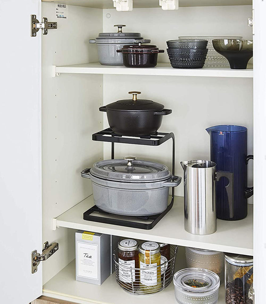 View 9 - Front view of black 2-Tier Pot Holder with Hooks holding pots in kitchen cabinet by Yamazaki Home.