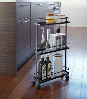 Black Rolling Cart holding oil and spices in kitchen by Yamazaki Home. view 6