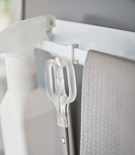 Close up view of white Magnetic Kitchen Towel  hook holding scissors, towel, and spray bottle by Yamazaki Home. view 7