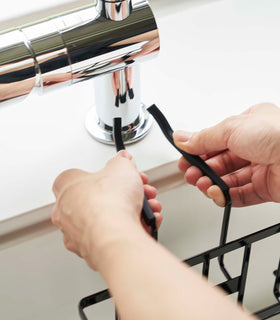 Close up of a Yamazaki Home black Faucet-Hanging Sponge Caddy being installed on a kitchen faucet view 10