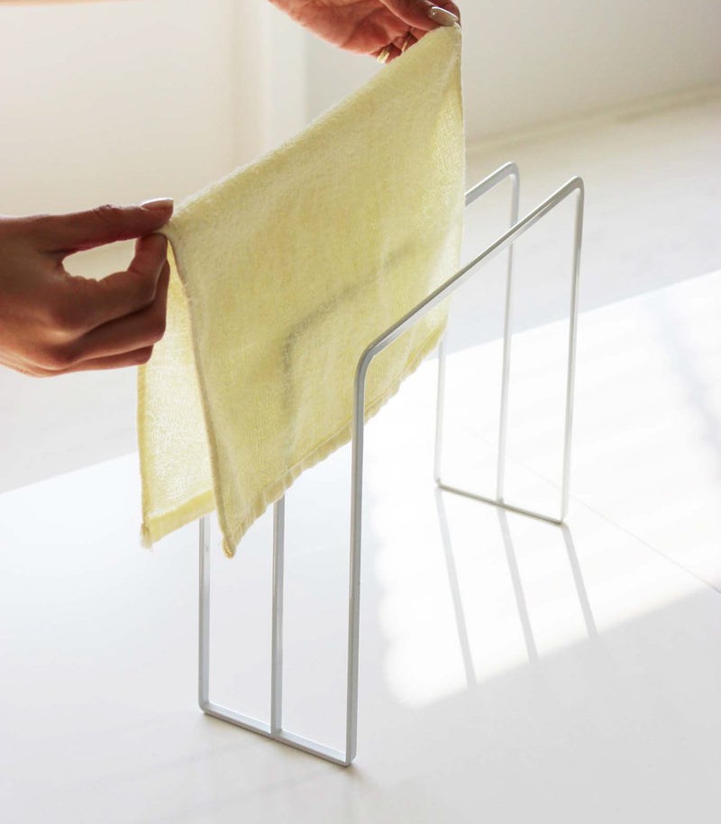 Close up view of white Dish Towel Holder holding towel on white countertop by Yamazaki Home.
