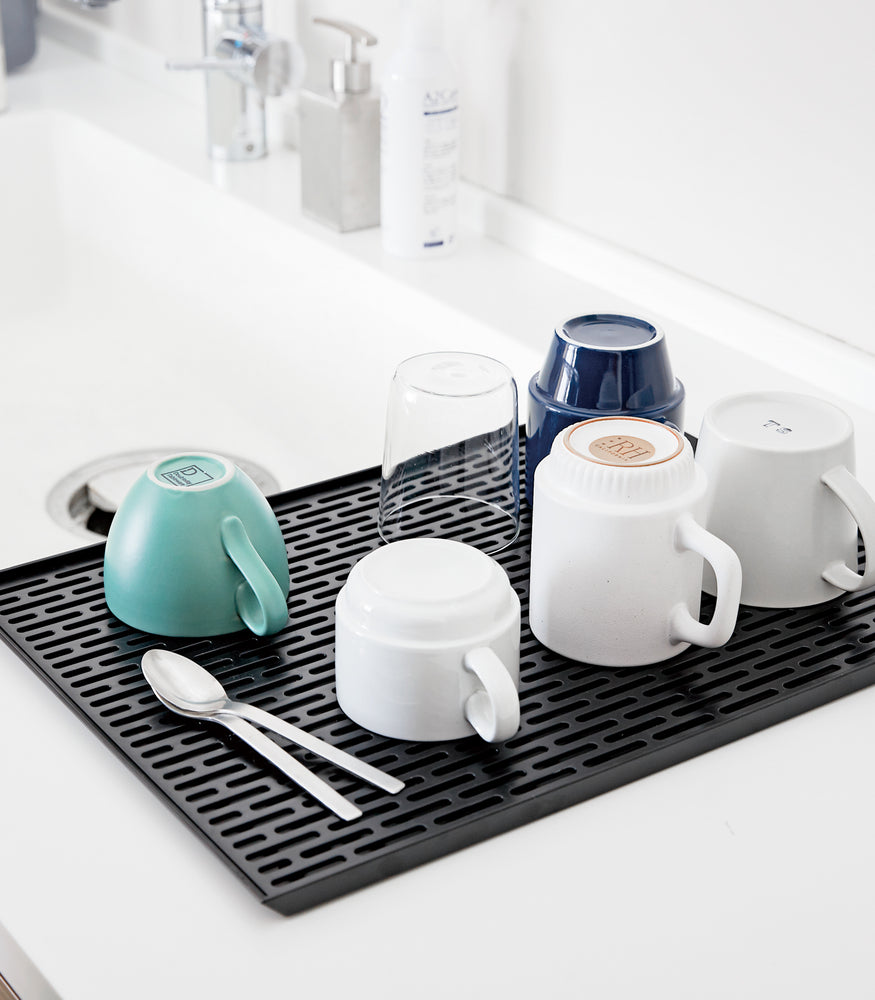 View 8 - Black Dish Drainer Tray holding cups on sink countertop by Yamazaki Home.