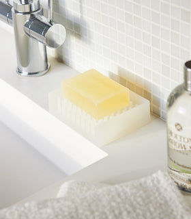 White Self-Draining Soap Dish holding soap bar on sink counter by Yamazaki Home. view 3