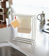 Front view of white Dish Towel Hanger holding towel and sponge on countertop by Yamazaki Home.
